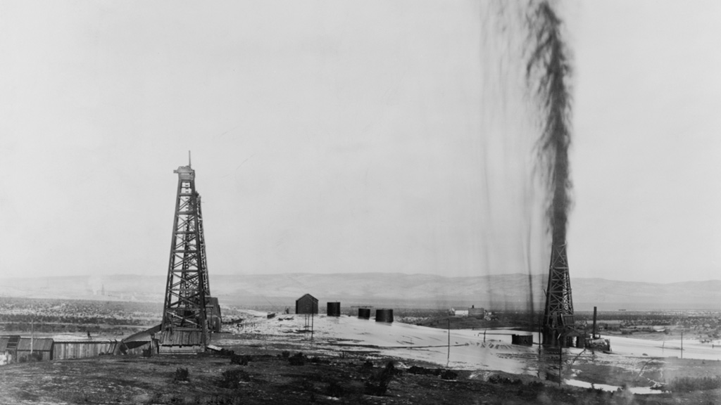 Black oil spews up into the air from an oil well and floods the surrounding ground