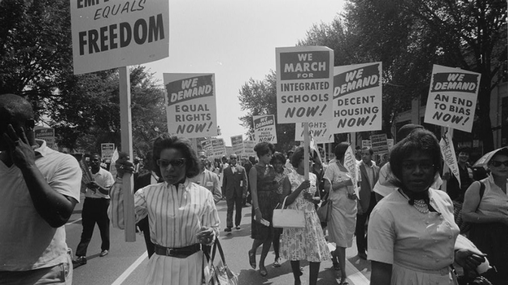 A procession of Black Americans carrying signs in support of equal rights, integrated schools, and decent housing