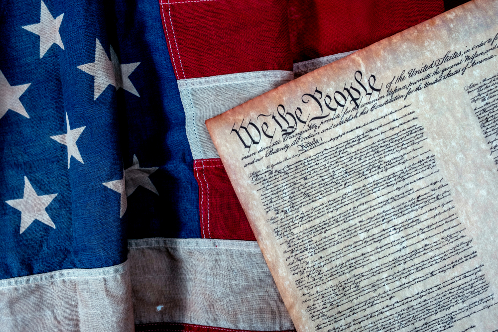 An image of the original U.S. Constitution is shown with a U.S. flag in the background