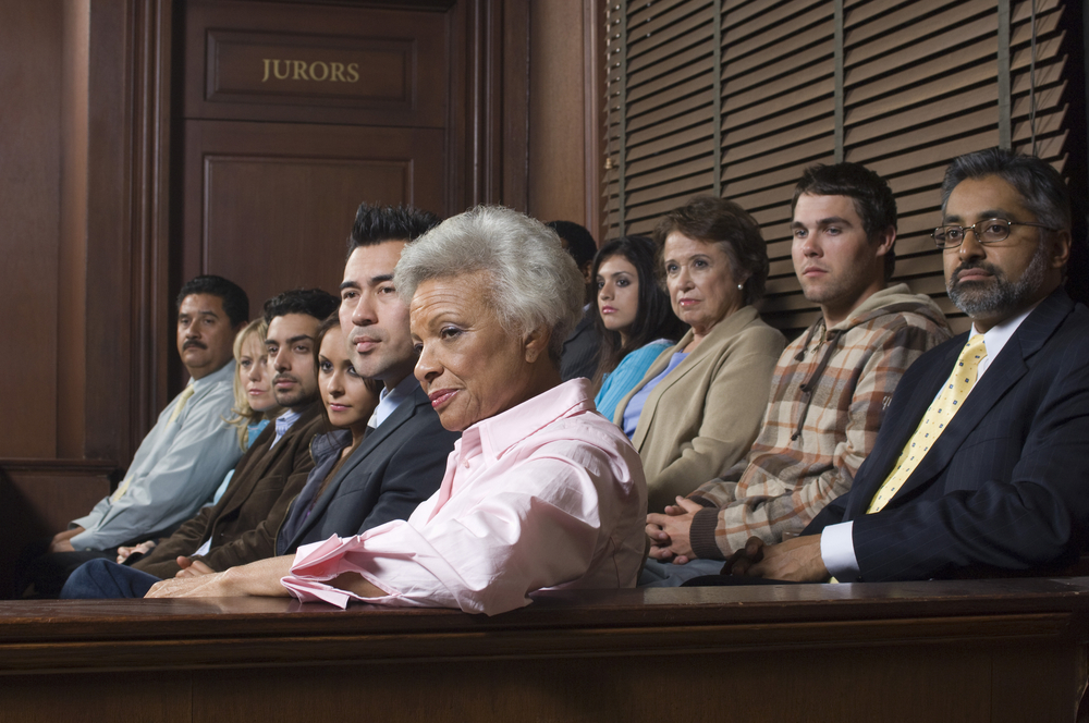 Twelve jurors are seated in a courtroom, all listening carefully.